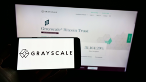 Person holding cellphone with logo of US crypto currency company Grayscale Investments LLC on screen in front of webpage. Focus on phone display. Unmodified photo. GBTC stock