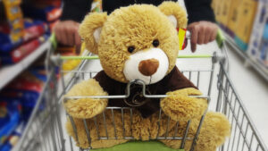 A stuffed teddy bear wearing a brown shirt in a grocery store shopping cart.