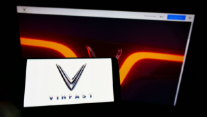Person holding mobile phone with logo of Vietnamese car manufacturer VinFast (VFS) on screen in front of business web page. Focus on phone display. Unmodified photo.