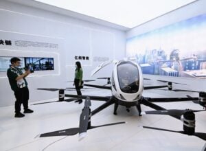 An image of a life-size white and black pilotable drone display in China, with a man in front of it taking a photo of a woman.