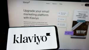 Person holding cellphone with logo of US marketing software company Klaviyo Inc. (KVYO) on screen in front of business webpage. Focus on phone display. Unmodified photo.