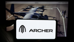 ウェブページの前の画面にアメリカの eVTOL 航空機会社 Archer Aviation Inc. (ACHR) のロゴが入った携帯電話を持っている人。 電話のディスプレイに注目してください。 無修正の写真。