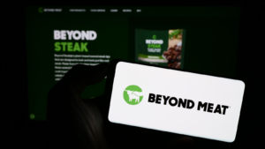 Person holding mobile phone with logo of American meat substitute company Beyond Meat Inc. (BYND) on screen in front of web page. Focus on phone display. Unmodified photo.