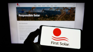 ウェブサイトの前の画面に米国の再生可能エネルギー会社 First Solar Inc. (FSLR) のロゴが表示されたスマートフォンを持っている人。 電話のディスプレイに注目してください。 無修正の写真。