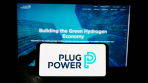 Person holding mobile phone with logo of American hydrogen fuel cell company Plug Power Inc. (PLUIG) on screen in front of webpage. Focus on phone display. Unmodified photo.