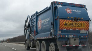 A picture of a blue Republic Services garbage truck driving on the highway on a cloudy day.