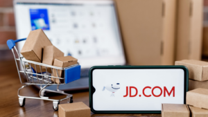 JD.com is a Chinese e-commerce company. Smartphone with JD.com logo on the screen, shopping cart and laptop. JD stock
