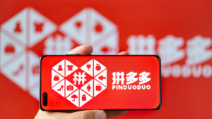 Man holding a mobile with PinDuoDuo (PDD) logo at horizontal composition.