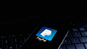 PayPal Holdings, Inc. (PYPL) icon displayed on smartphone with keyboard background. is an American multinational financial technology company operating an online payment