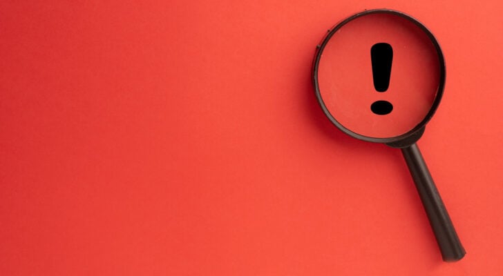 Black exclamation point with magnifying glass on top of it, all against a red background and representing warning