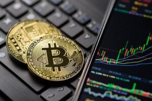 An image of two Bitcoin on a laptop, next to a rising graph on a phone screen