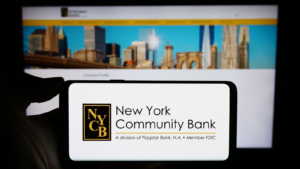 Person holding cellphone with logo of US company New York Community Bancorp Inc. (NYCB) in front of business webpage. Focus on phone display. Unmodified photo.