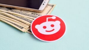 Reddit (RDDT) paper logo lies with envelope full of dollar bills and smartphone. Reddit IPO