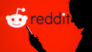 Un bărbat cu siluetă care folosește un smartphone cu sigla Reddit (RDDT) pe fundal neclar este un site american de agregare de știri sociale, de evaluare a conținutului și de discuții.