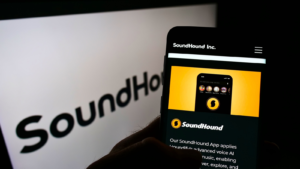 Person holding smartphone with webpage of US audio recognition company SoundHound Inc. (SOUN) on screen in front of logo. Focus on center of phone display. Unmodified photo.