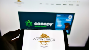 Person holding cellphone with business logo of Canadian cannabis company Canopy Growth Corp. (CGC) on screen in front of webpage. Focus on phone display. Unmodified photo.