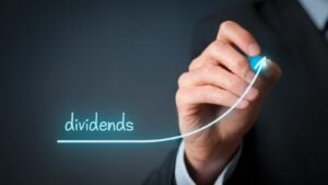 The word "dividends" written over a blue graph line being drawn by a business person's hand
