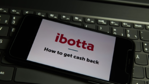 Closeup of mobile phone screen with logo lettering of ibotta (IBTA) cashback app on computer keyboard (focus on left letter t upper lettering)