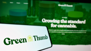 The logo for Green Thumb Industries Inc (GTBIF) is displayed on a smartphone in front of a screen displaying their website.