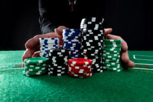 A photo showing a man pushing a large stack of various poker chips on a poker table.