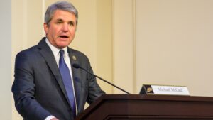 A photo of Michael McCaul standing at a podium in front of a cream wall.