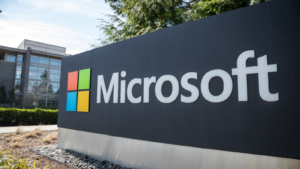 Wide-angle shot of a Microsoft sign at the headquarters of a company that produces PCs and cloud computing, with an office building in the background. MSFT stock