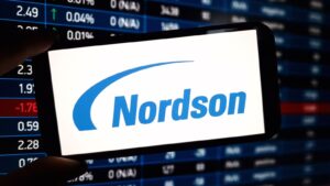 A smartphone displaying the Nordson (NDSN) logo in front of a trading screen.
