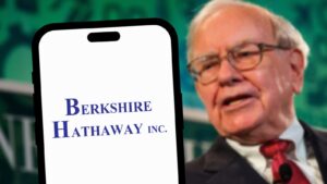 Warren Buffett in the background behind a phone displaying the Berkshire Hathaway logo