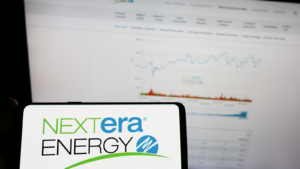 Person holding mobile phone with logo of American energy company NextEra Energy Inc. on screen in front of web page. NEE stock