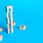 Wooden blocks on a bright blue background that create a blue arrow pointing up.