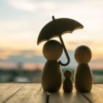 A concept image showing a wooden family with an umbrella protecting them. Meant to represent life insurance.