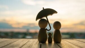 A concept image showing a wooden family with an umbrella protecting them. Meant to represent life insurance.