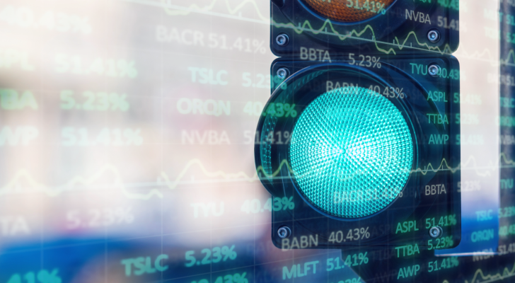 A green light overlaid with a screen of stock tickers to signify the Federal Reserve giving investors the green light to buy stocks