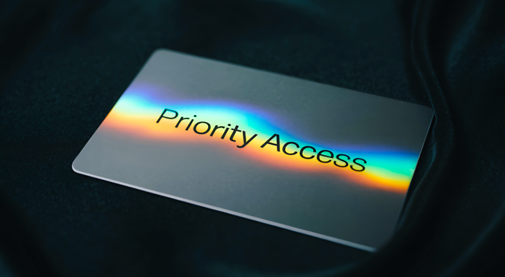 A sleek metallic card with the words priority access illuminated by a vibrant holographic rainbow spectrum against a dark textured background, representing the new Nasdaq fast entry rule